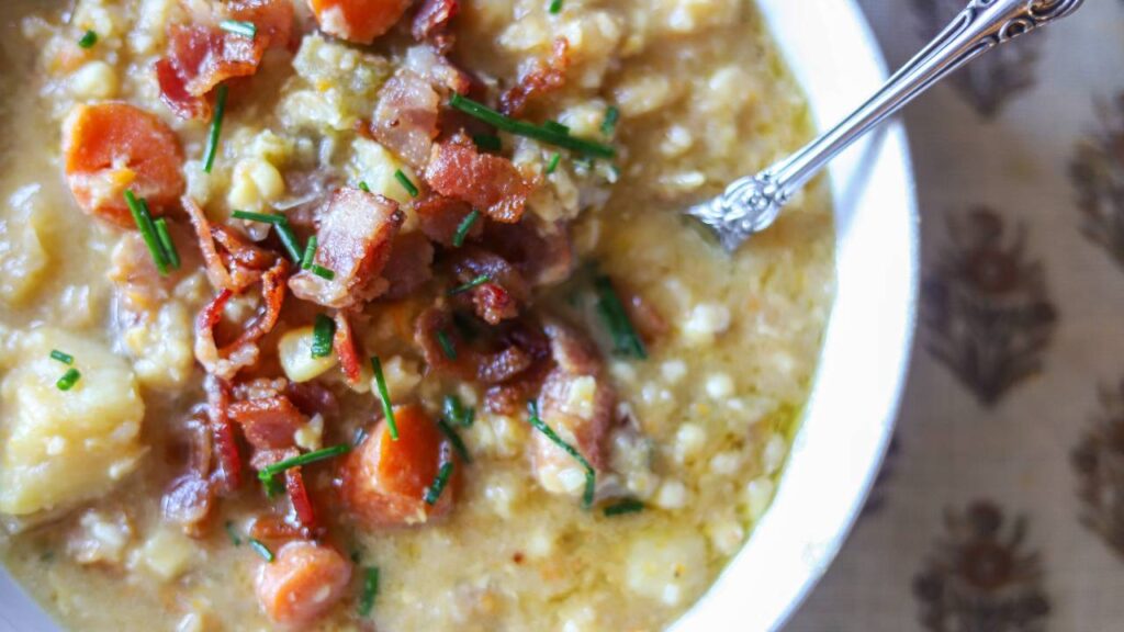 Close-up of corn chowder showing chopped carrots, potatoes, and crispy bacon bits.