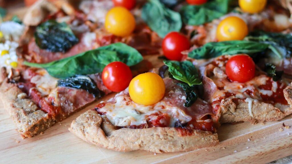 Side view of homemade pizza showing the texture of the crust and colorful toppings like fresh basil and cherry tomatoes.