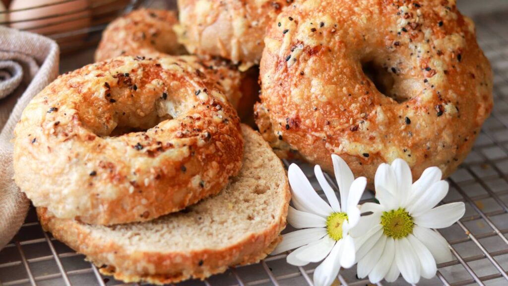 closeup of homemade freshly milled sourdough bagels cut in half with everything bagel seasoning sprinkled on top.