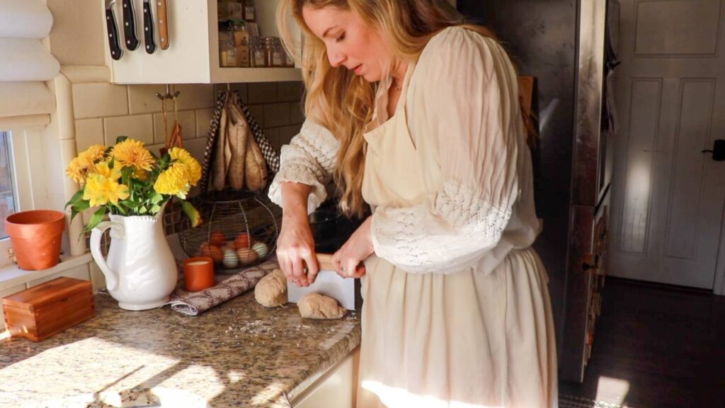 woman standing at a kitchen counter cutting through bagel dough