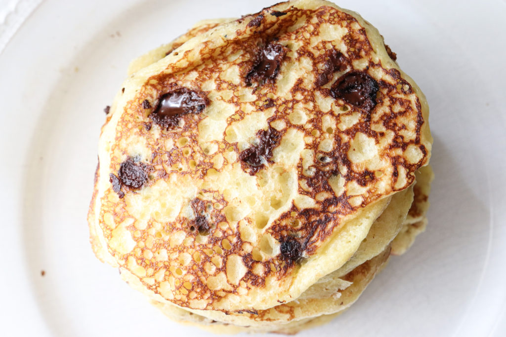 Stack of fluffy sourdough chocolate chip pancakes on a white plate.