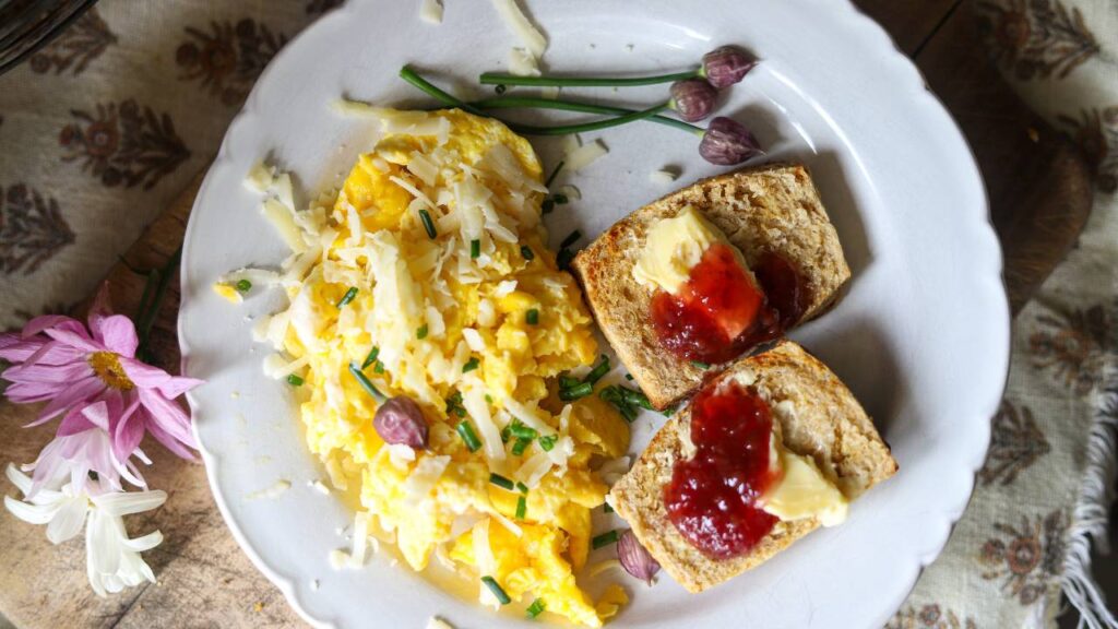 Overhead view of scrambled eggs and toast with jam and butter on a plate.