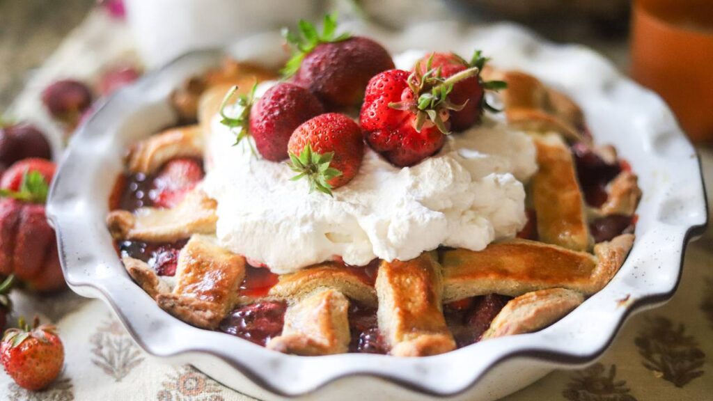 Strawberry pie topped with whipped cream and fresh strawberries on a rustic table.