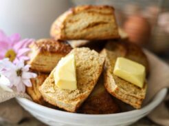 Flaky homemade biscuits with butter in a white bowl and fresh flowers.
