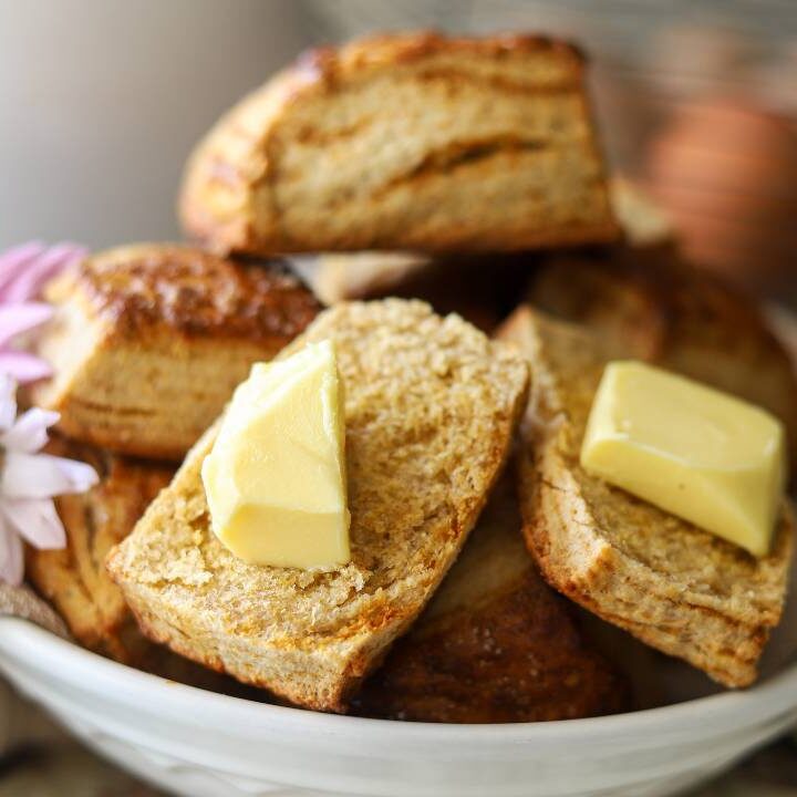 Flaky homemade biscuits with butter in a white bowl and fresh flowers.