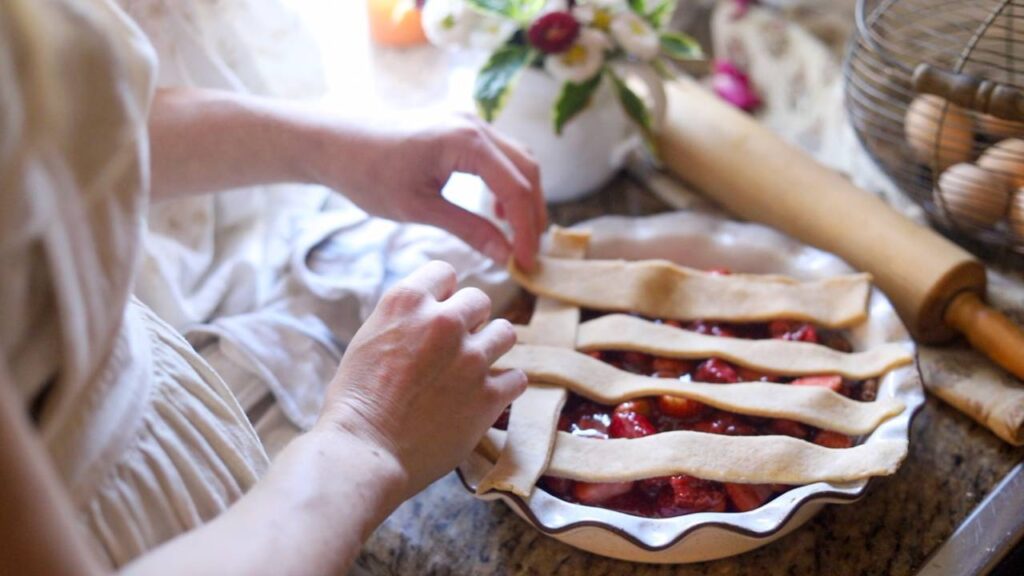 Placing lattice strips of pie crust over strawberry filling in a pie dish.