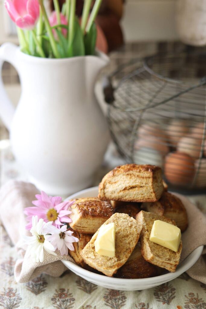 Bowl of biscuits with butter and flowers on a table.
