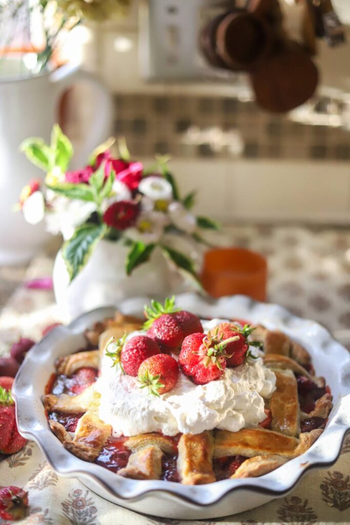 Strawberry pie topped with whipped cream and fresh strawberries on a floral tablecloth.