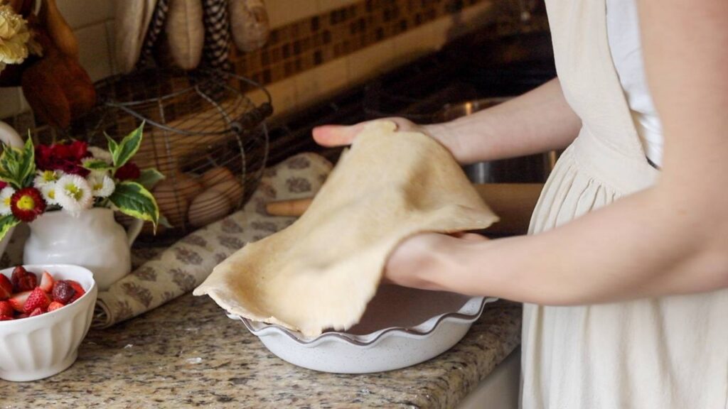Woman laying pie dough into a ceramic pie dish.