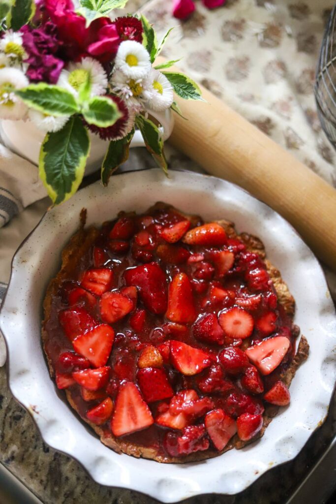 Unbaked strawberry pie with glossy strawberry filling in a white pie dish beside a bouquet.