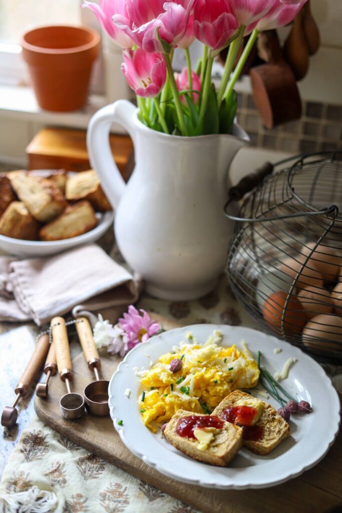 Breakfast plate with scrambled eggs and buttered toast next to a pitcher of tulips.