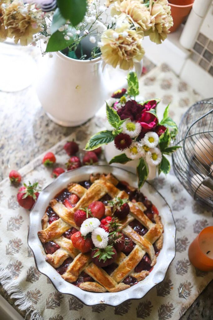 Strawberry pie topped with whipped cream and fresh strawberries on a floral tablecloth.