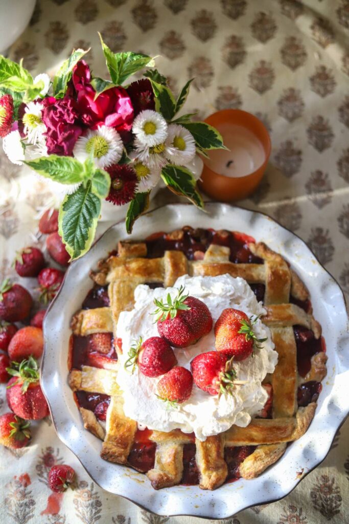Strawberry pie topped with whipped cream and fresh strawberries on a floral tablecloth.