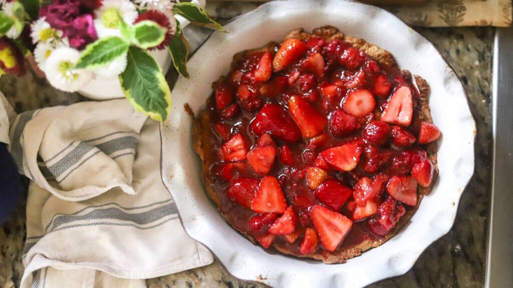 Overhead view of unbaked strawberry pie filled with strawberry mixture next to a striped towel.