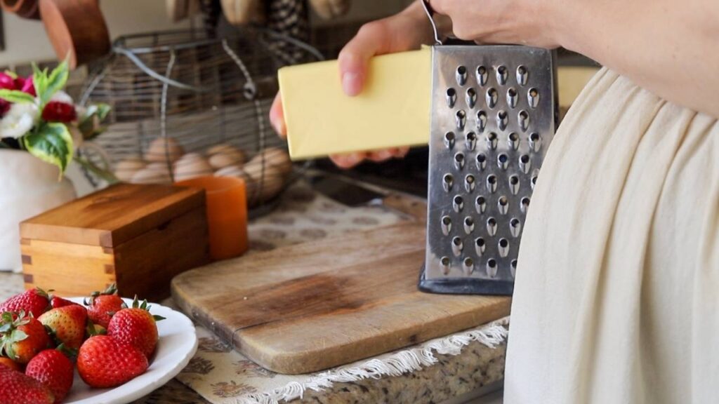 Grating butter on a box grater beside a plate of strawberries.