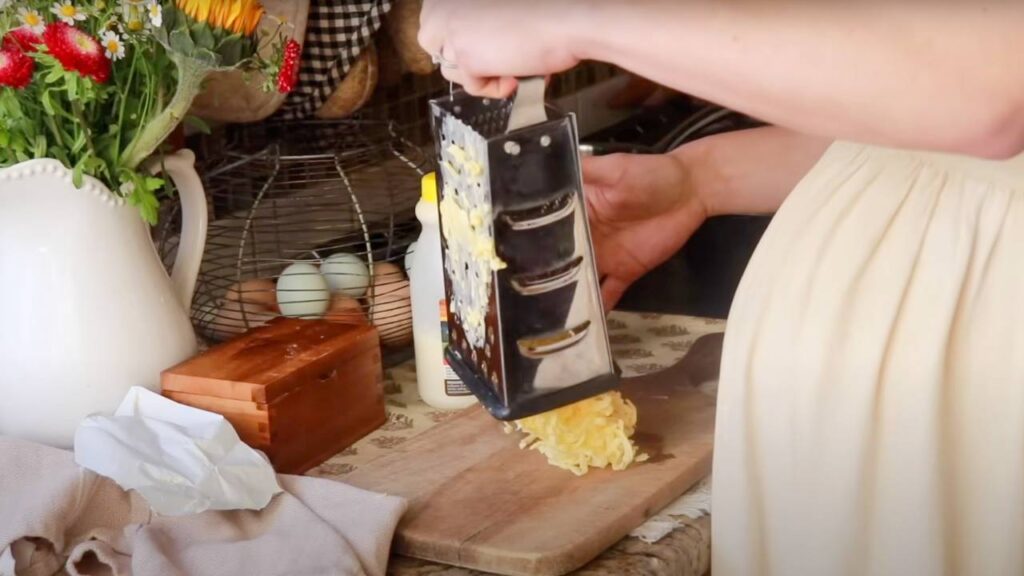 Woman grating biscuit ingredients on a wooden cutting board.