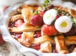Strawberry pie topped with whipped cream and fresh strawberries on a rustic table.