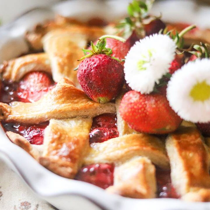 Strawberry pie topped with whipped cream and fresh strawberries on a rustic table.