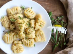 Cooked gnocchi on a white plate with herbs and a daisy nearby.