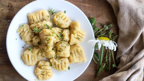 Cooked gnocchi on a white plate with herbs and a daisy nearby.