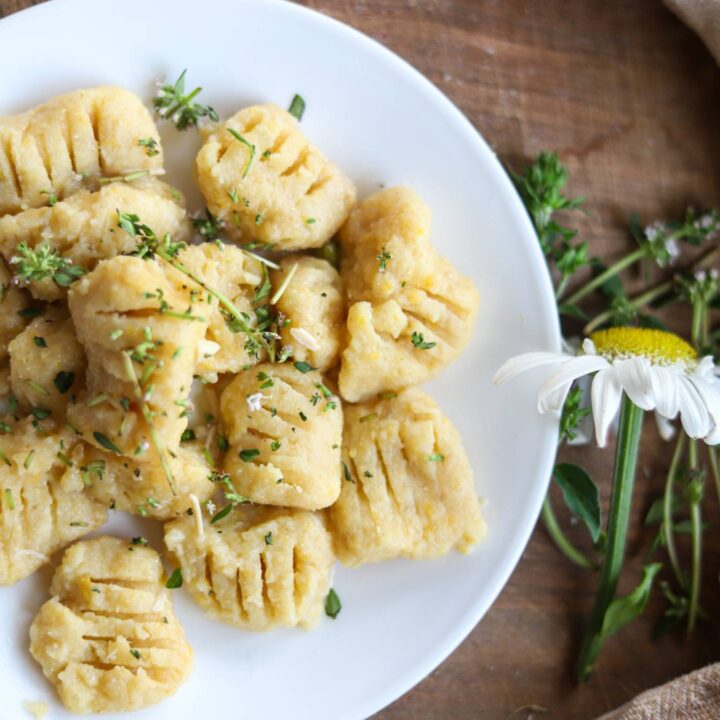 Cooked gnocchi on a white plate with herbs and a daisy nearby.