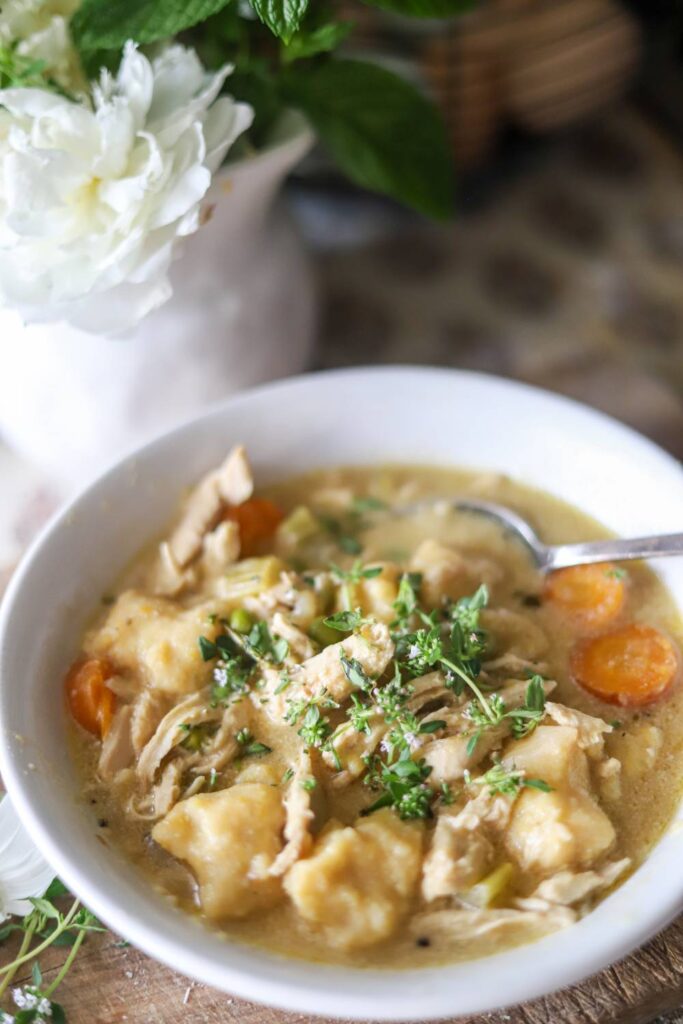 Chicken gnocchi soup next to a white flower in a cozy kitchen setting.