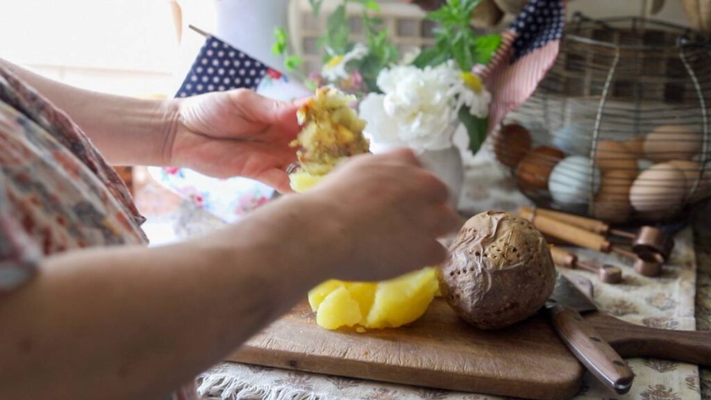 Hands peeling cooked potatoes on a cutting board.