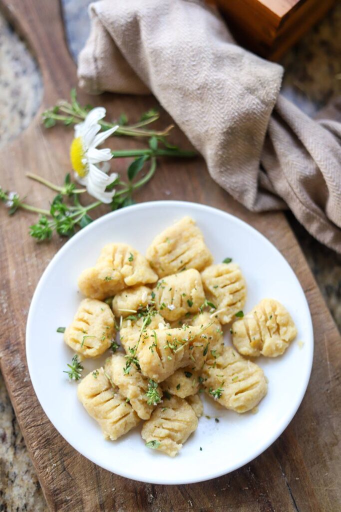 Plate of homemade gnocchi with herbs beside a daisy and linen napkin.