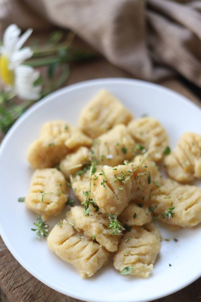 Close-up of gnocchi on a white plate topped with fresh herbs.