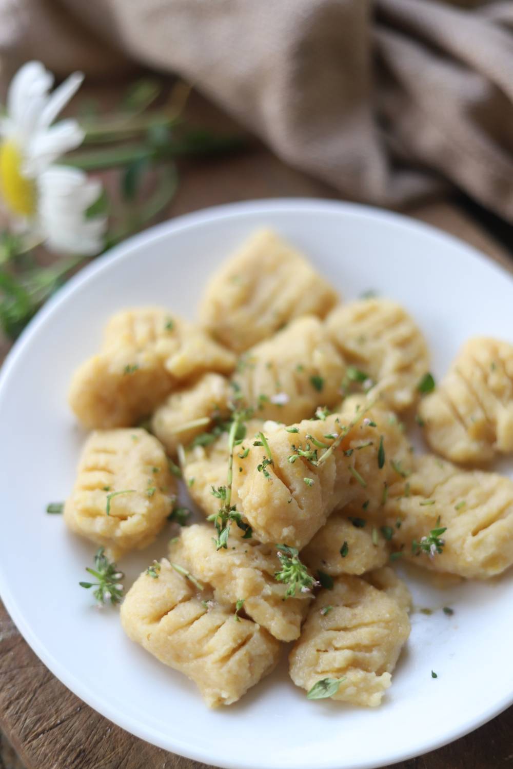 Close-up of gnocchi on a white plate topped with fresh herbs.