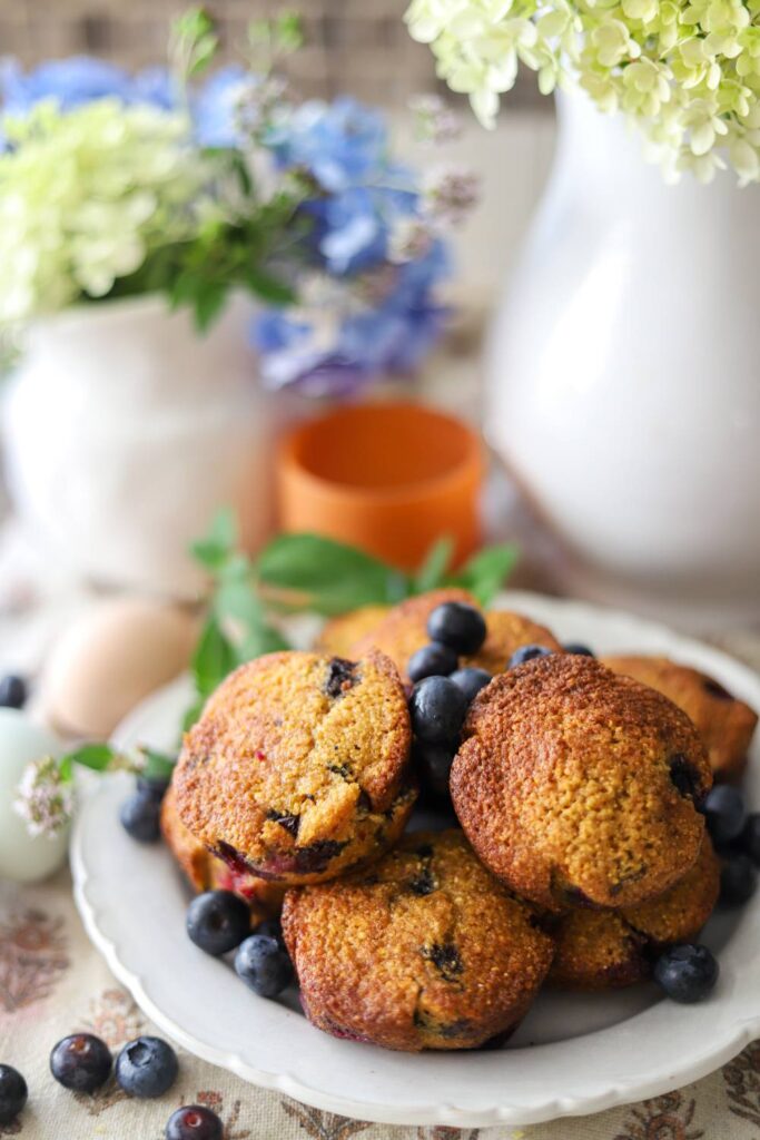 Stack of blueberry muffins on a plate with fresh blueberries.