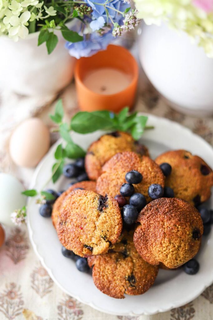 Top-down view of blueberry muffins with eggs and flowers nearby.