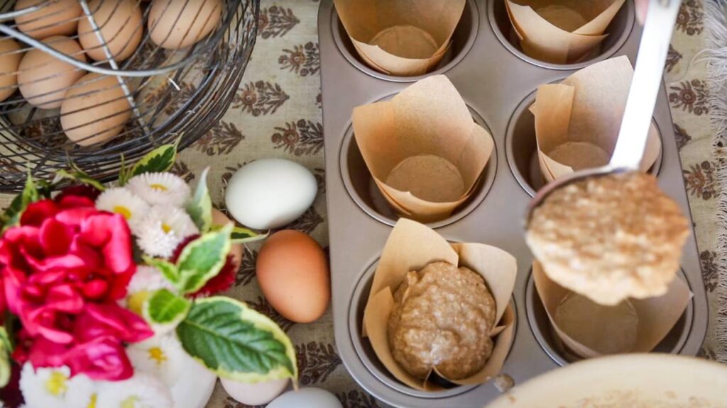 Muffin batter being scooped into parchment-lined muffin tin.