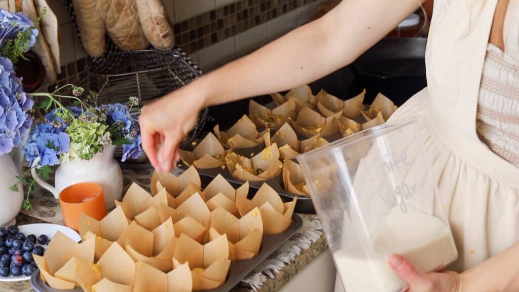Woman sprinkling sugar into muffin liners.