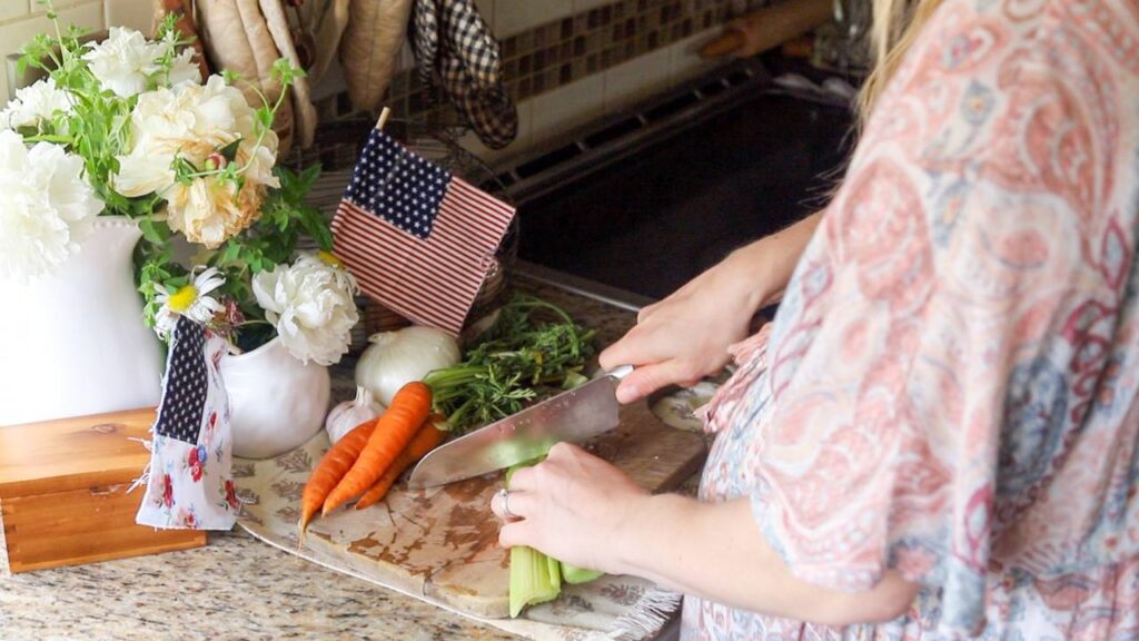 Chopping celery and carrots on a kitchen counter with flowers and flags.