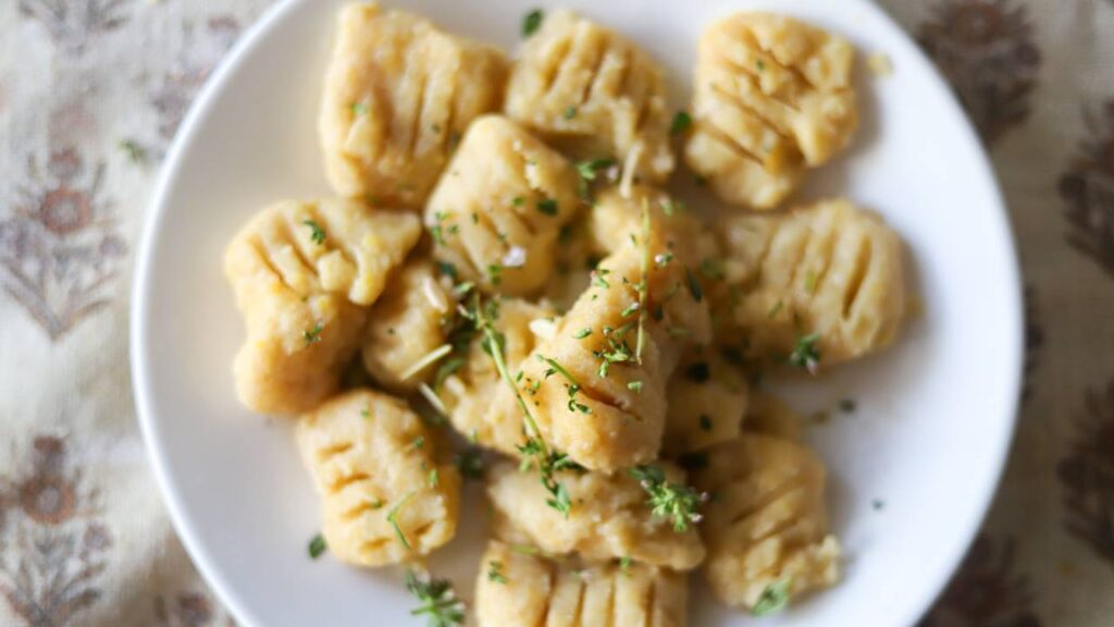 Top-down view of plated gnocchi garnished with fresh herbs.