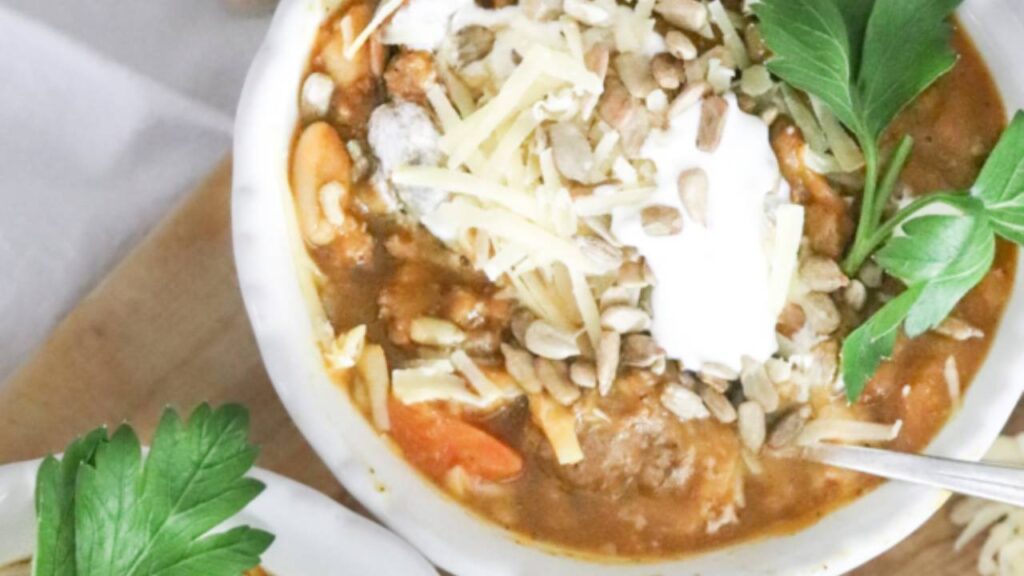 Bowl of pumpkin chili topped with cheese, sour cream, and seeds