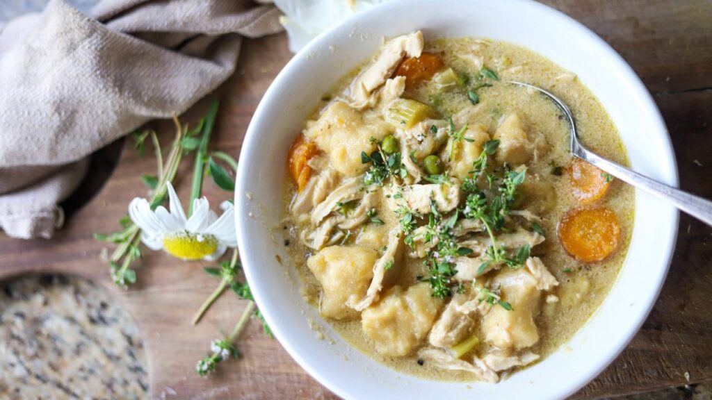 Bowl of chicken gnocchi soup with vegetables and herbs.