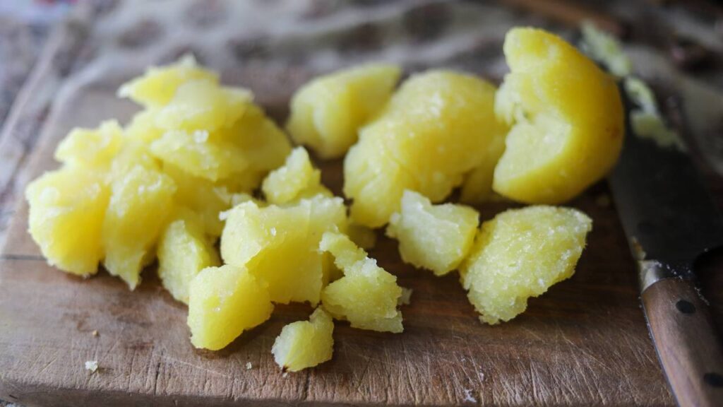 Chopped boiled potatoes on a wooden cutting board.