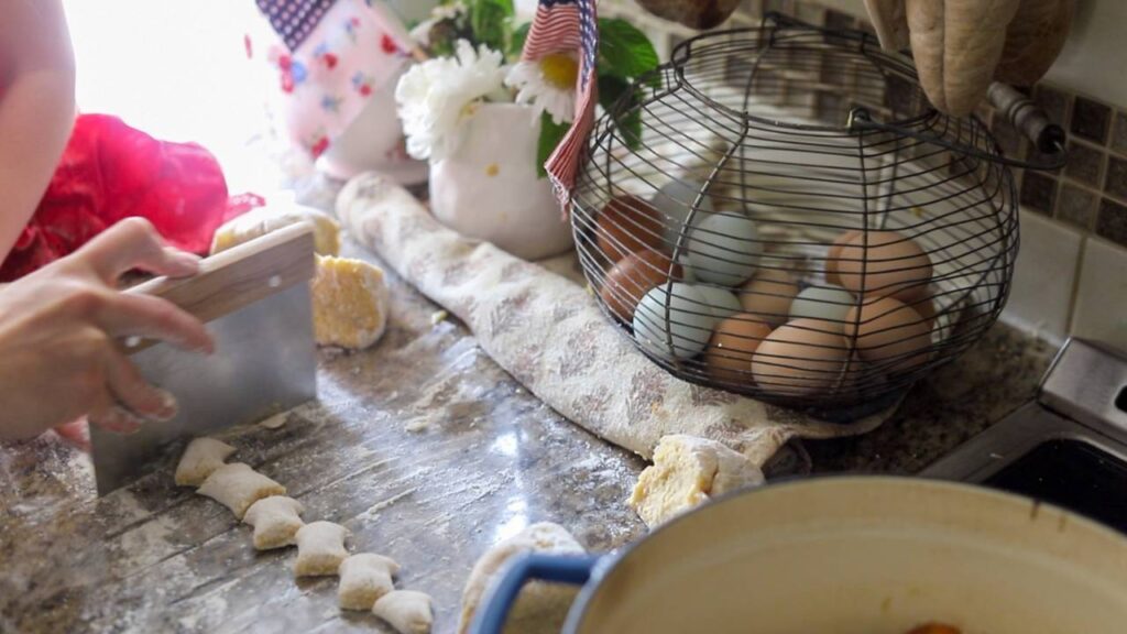 Hand cutting gnocchi dough into pieces next to a basket of eggs.