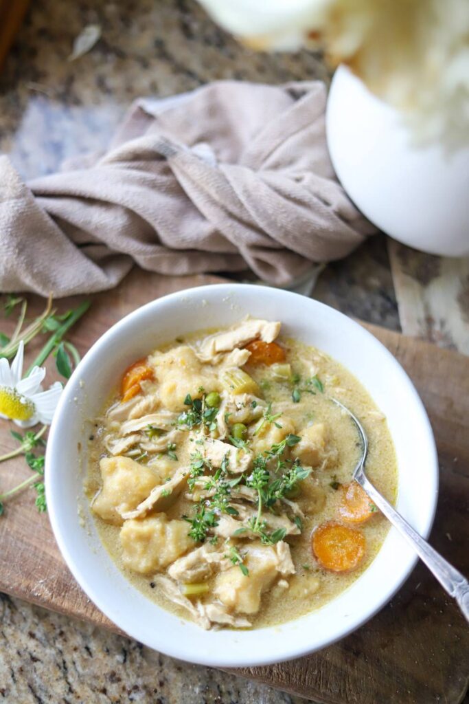 Overhead shot of chicken gnocchi soup with a towel and flowers nearby.