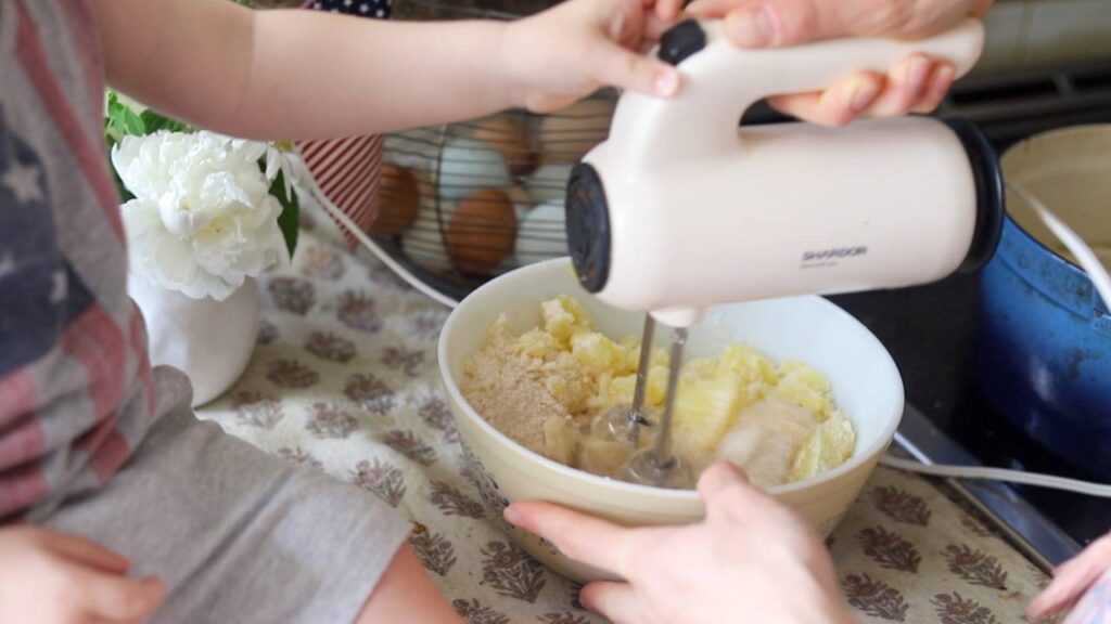 Child helping mix gnocchi ingredients in a bowl with a hand mixer.
