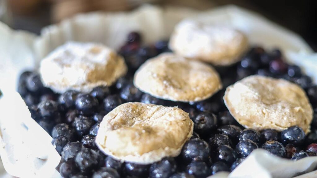 Unbaked biscuit dough placed on top of fresh blueberries in a dish