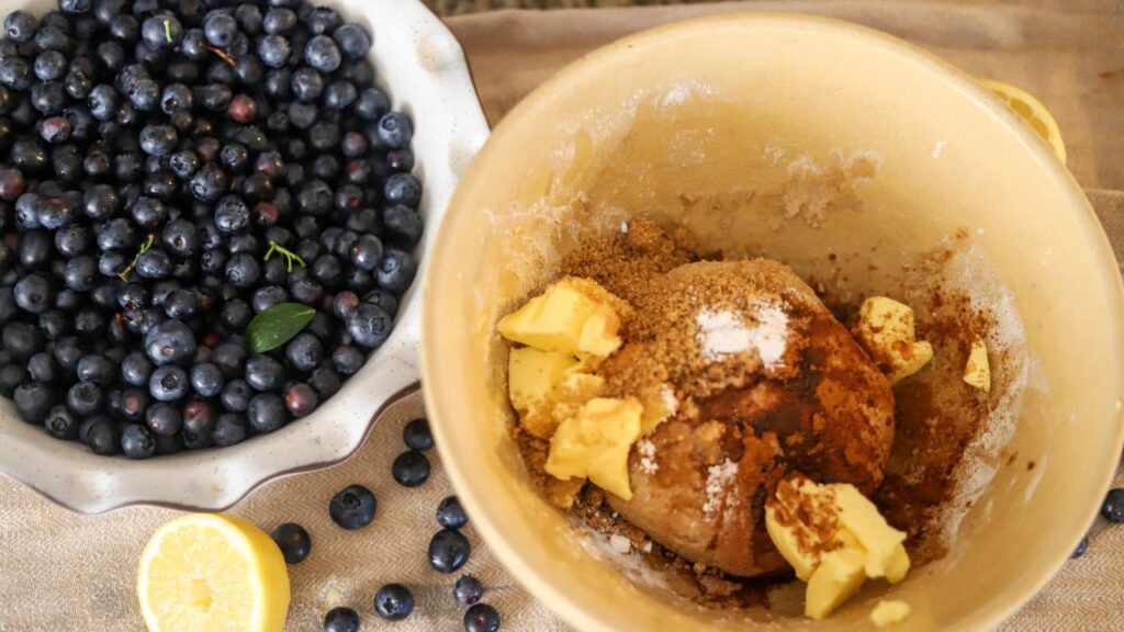 Bowl of dough with brown sugar, cinnamon, and butter next to a dish of fresh blueberries
