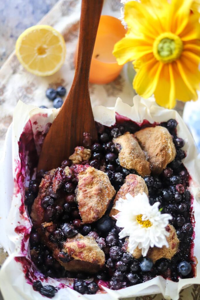 Overhead view of baked blueberry cobbler in a parchment-lined dish with a wooden spoon