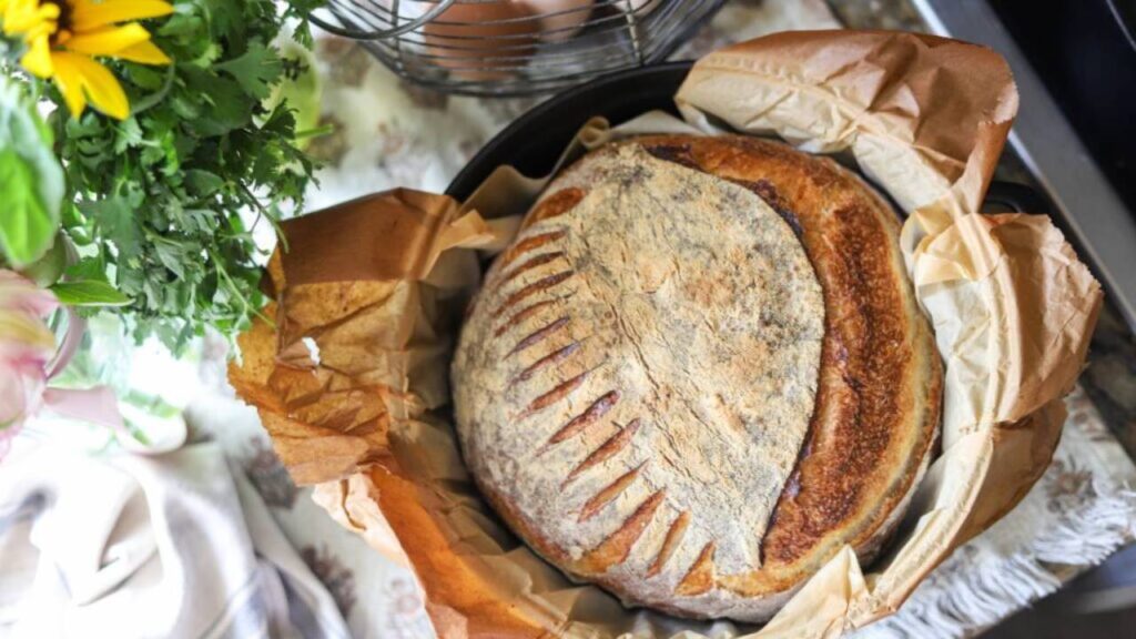 Round sourdough loaf in parchment-lined Dutch oven