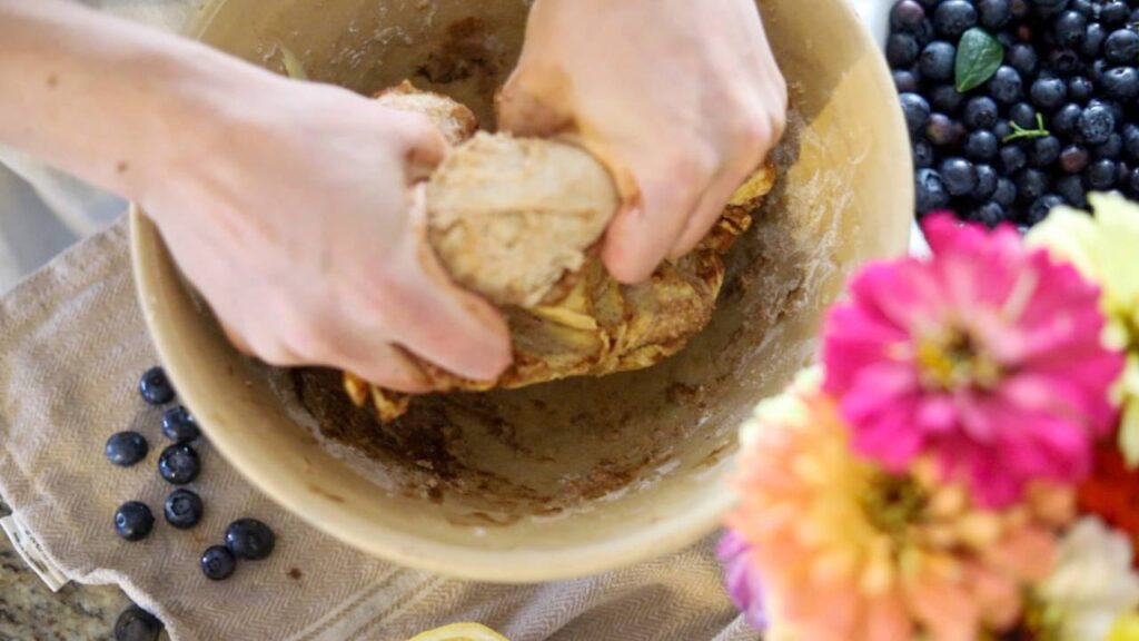 Hands kneading dough in a large mixing bowl next to fresh blueberries