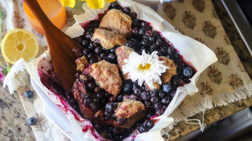 Freshly baked blueberry cobbler in a white dish topped with a flower