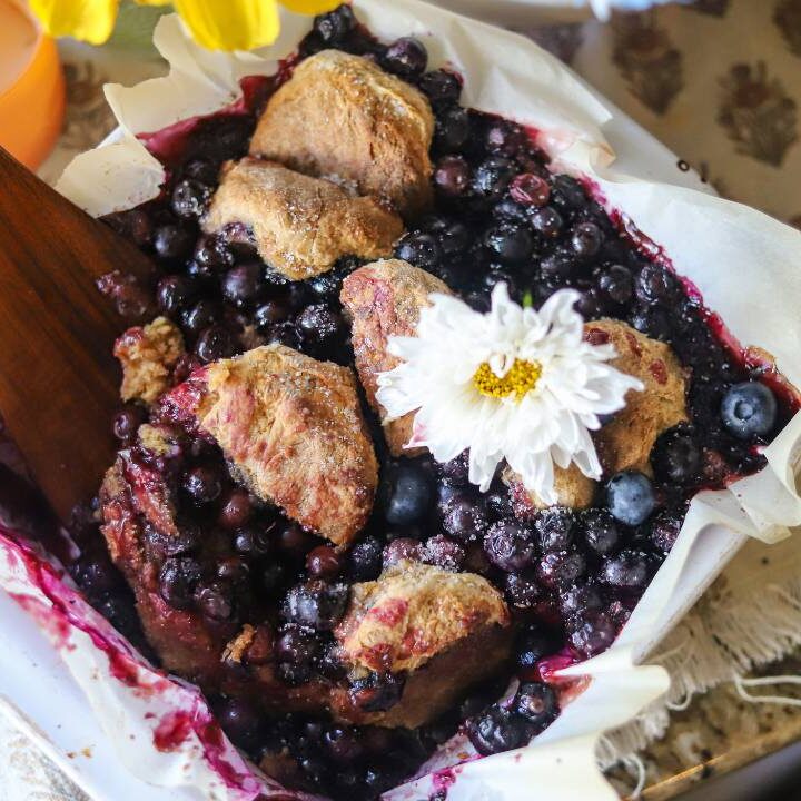 Freshly baked blueberry cobbler in a white dish topped with a flower