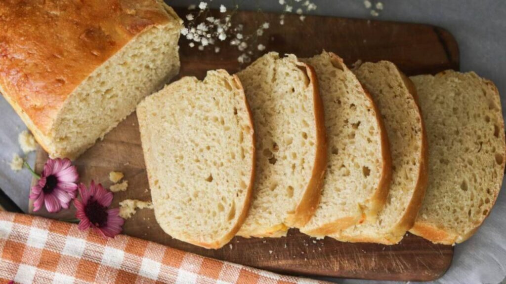 Sliced loaf of sourdough bread on wooden board with flowers